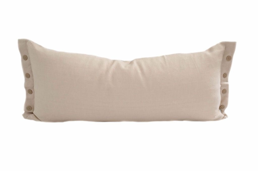 A cream lumbar pillow with brown buttons on the ends of it.
