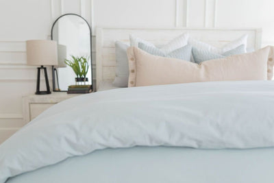 A bed made with a light blue zipper duvet folded half way down the bed and adorned with neutral and light blue pillows.