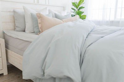 A brightly lit bedroom with a bed made with light gray waffle textured zipper bedding and a light blue zipper duvet partially folded half way down the bed and adorned with neutral pillows.