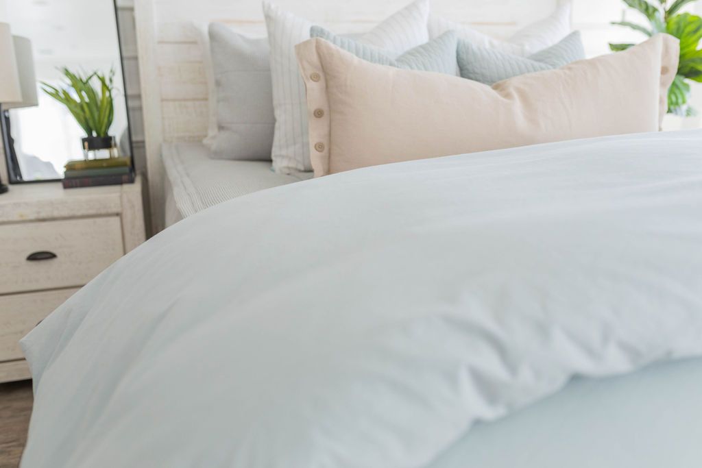 A close up view of a bed made with light gray waffle textured zipper bedding and a light blue zipper duvet folded half way down the bed and adorned with neutral pillows.