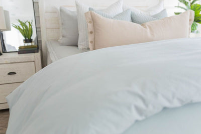A close up view of a bed made with light gray waffle textured zipper bedding and a light blue zipper duvet folded half way down the bed and adorned with neutral pillows.