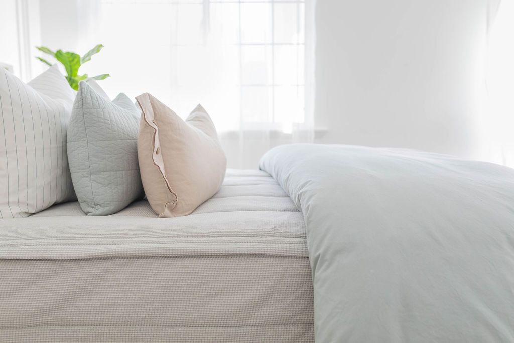 A side view of a bed made with light gray waffle textured zipper bedding and a light blue zipper duvet folded half way down the bed and adorned with neutral pillows.