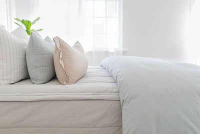 A side view of a bed made with light gray waffle textured zipper bedding and a light blue zipper duvet folded half way down the bed and adorned with neutral pillows.