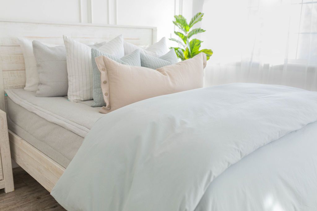A brightly lit bedroom with a bed made with light gray waffle textured zipper bedding and a light blue zipper duvet folded half way down the bed and adorned with neutral pillows.