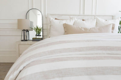 A bed made with a woven ivory and tan striped zipper duvet folded half way down the bed and adorned with neutral pillows.