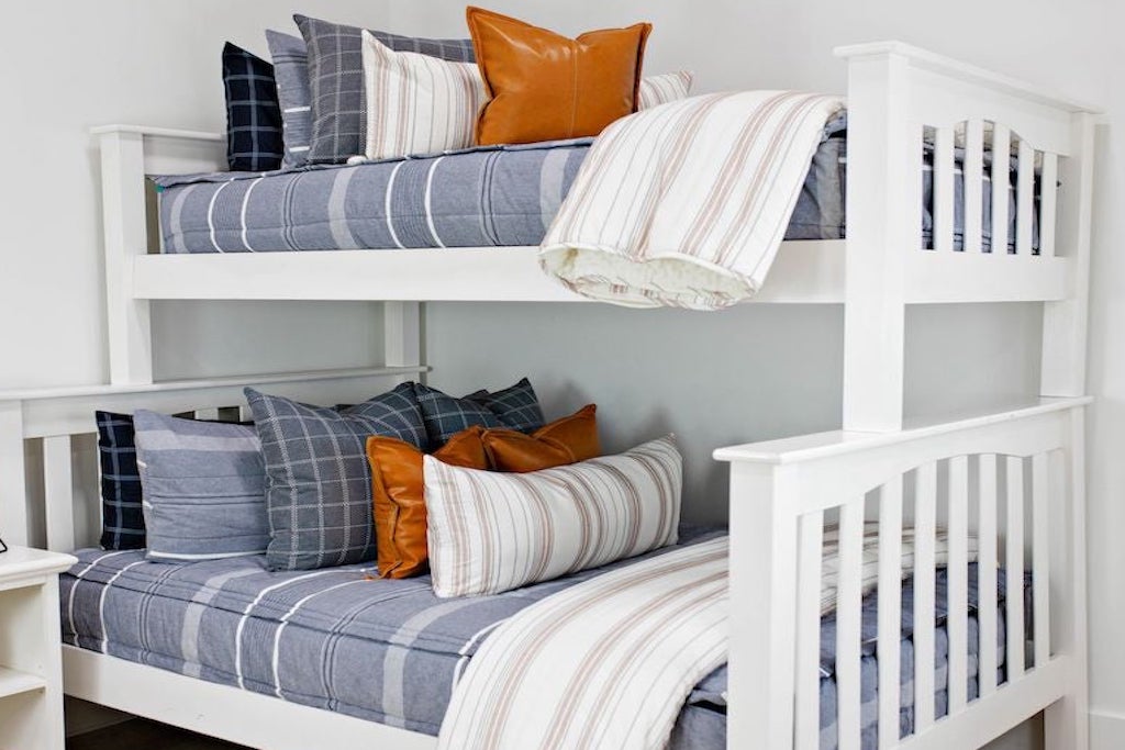 queen bed with Deep navy woven stripe bedding with deep navy striped euros, faux leather pillows, white and black grid pillow, and white textured blanket with braided tassels