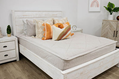 White queen bed with beige textured bedding, cream textured euro pillows, medium peach textured pillows and a boho rainbow lumbar pillow.  