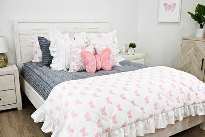 White queen bed with gray and white textured bedding, white and pink striped pillows, white and pink butterfly pillows, a pink butterfly shaped pillow and a white and pink butterfly blanket.  