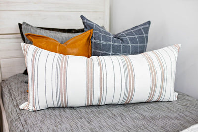 Enlarged view of a blue gray and white grid pillow, a brown leather pillow, and a cream and cognac striped lumbar pillow.  