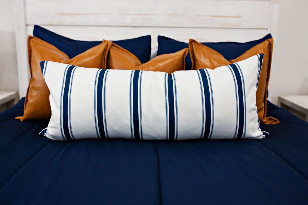 Enlarged view of navy blue bedding, medium brown leather pillows and a white and navy blue striped lumbar pillow.