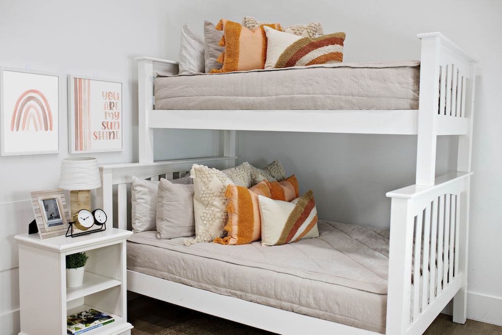 White bunk beds with beige textured bedding, cream textured euro pillows, medium peach textured pillows and a boho rainbow lumbar pillow.  