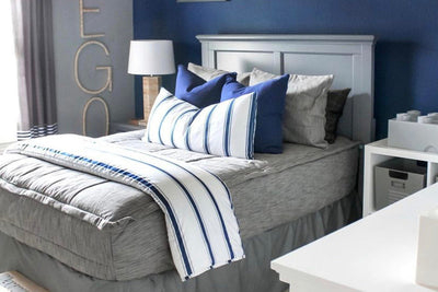 gray twin bed frame with Brown and gray woven textured bedding and two navy euros, white XL lumbar with navy vertical stripes, and white blanket with horizontal navy stripes at the foot of the bed