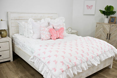 White queen bed with white textured bedding, white and pink striped pillows, white and pink butterfly pillows, a pink butterfly shaped pillow and a white and pink butterfly blanket.  