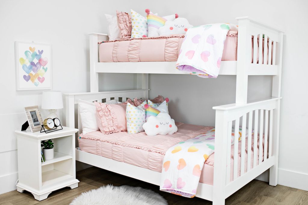 White bunk beds with blush pink ruffled bedding, medium rainbow heart pillows, medium white rainbow pillows, a white cloud pillow and a white and rainbow heart blanket.  