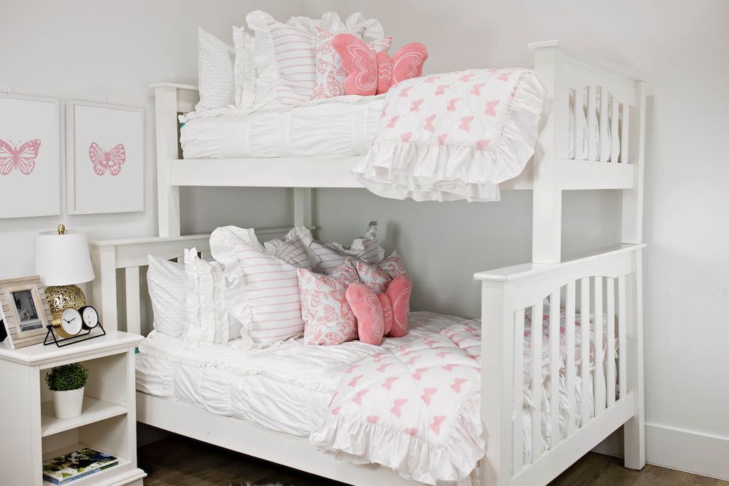 White bunk beds with white textured bedding, white and pink striped pillows, pink and white butterfly pillows, a pink butterfly shaped pillow and a white and pink butterfly blanket.  