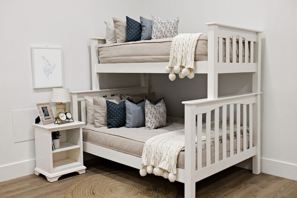 White bunk beds with beige textured bedding, blue and white spotted pillows, blue and white polka dot pillows, white and gray floral pillows and a cream throw.  