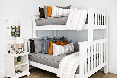 White bunk beds with gray and brown woven bedding, blue gray and white plaid pillows, cream and cognac striped lumbar pillows and cream and cognac striped blankets.