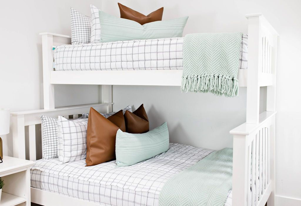 White bunk bed with white and black grid patterned bedding, faux leather euro pillows, sage green extra long lumbar pillow and sage green chenille textured throw