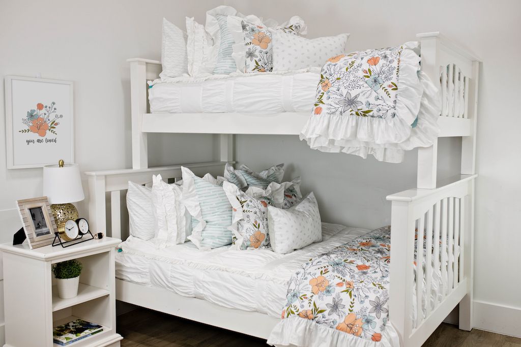 White bunk beds with white textured bedding, white and blue striped pillows, multicolored floral pillows, a gray and white lumbar pillow and a multicolored floral blanket.  