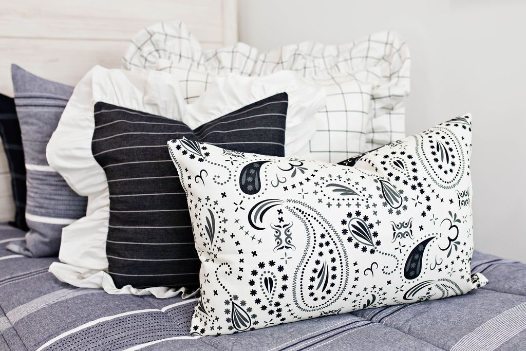 cream and black grid euro with ruffle along the edge, charcoal striped pillow with white ruffle along the edge, cream lumbar with charcoal paisley print