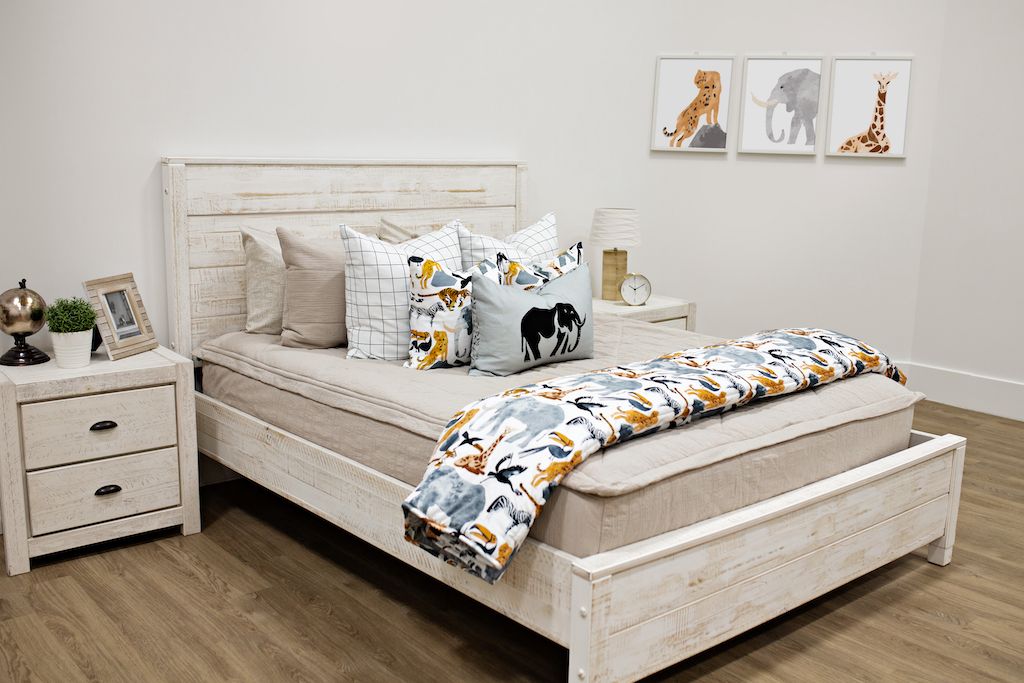 White queen bed with beige textured bedding, white and black grid pillows, jungle animal pillows, a gray lumbar pillow with an elephant and a blanket with jungle animals.  