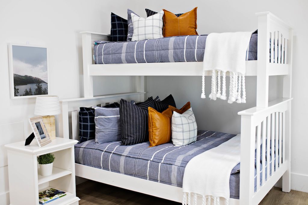 bunk bed with blue and navy striped bedding and deep navy striped euros, faux leather pillows, white and black grid pillow, and white textured blanket with braided tassels