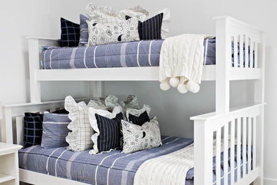 White bunk bed with blue striped bedding, cream and black striped euros with ruffle along the edge, charcoal striped pillow with white ruffle along the edge, cream lumbar with charcoal paisley print, and cream textured blanket with pom poms