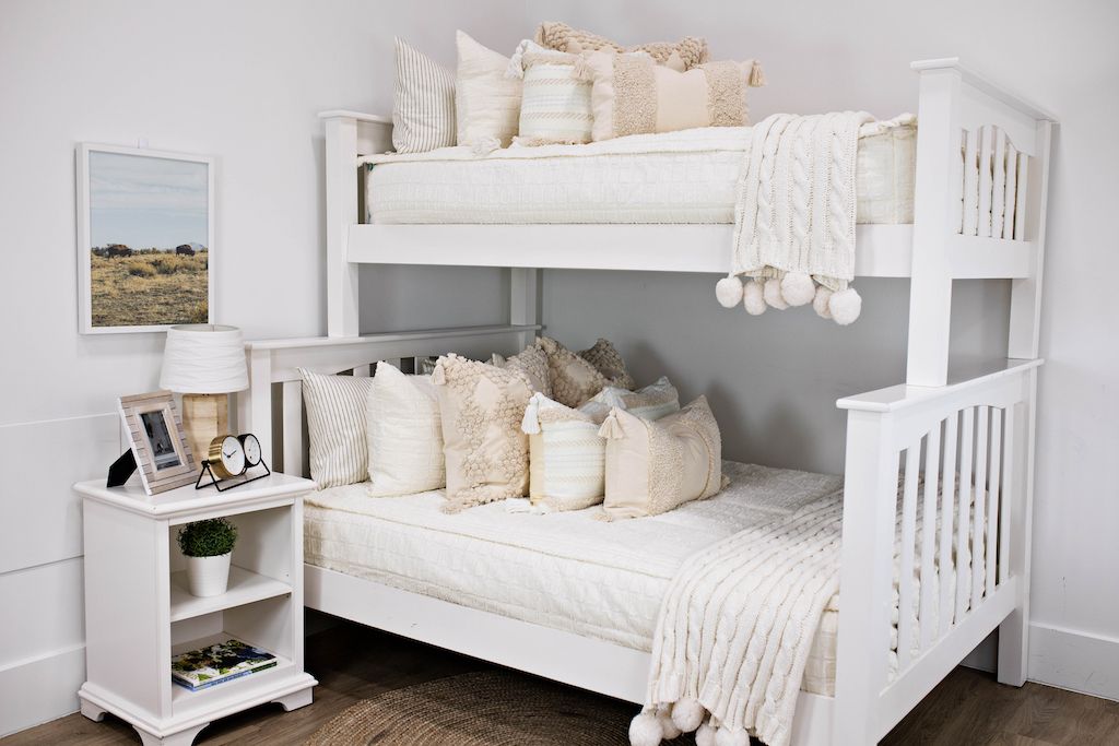 white bunk bed with dark creamy textured euro, a cream and tan woven textured pillow and a textured dark creamy lumbar with tassels with an off white braided throw with pom poms along the edge and desert buffalo artwork on wall