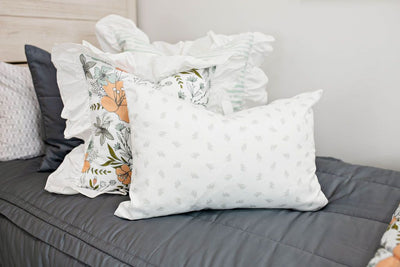 Enlarged view of a twin bed with gray bedding, a white and blue striped pillow, a multicolored floral pillow and a gray and white lumbar pillow. 