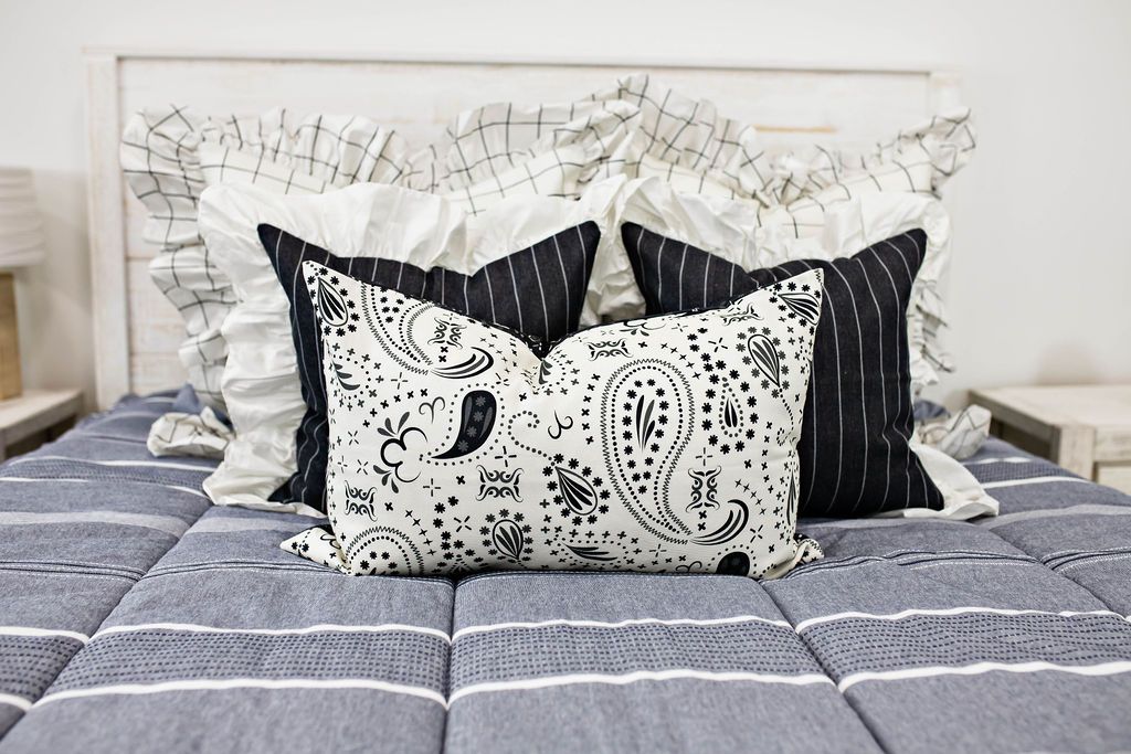 two cream and black grid euro with ruffle along the edge, two charcoal striped pillow with white ruffle along the edge, cream lumbar with charcoal paisley print