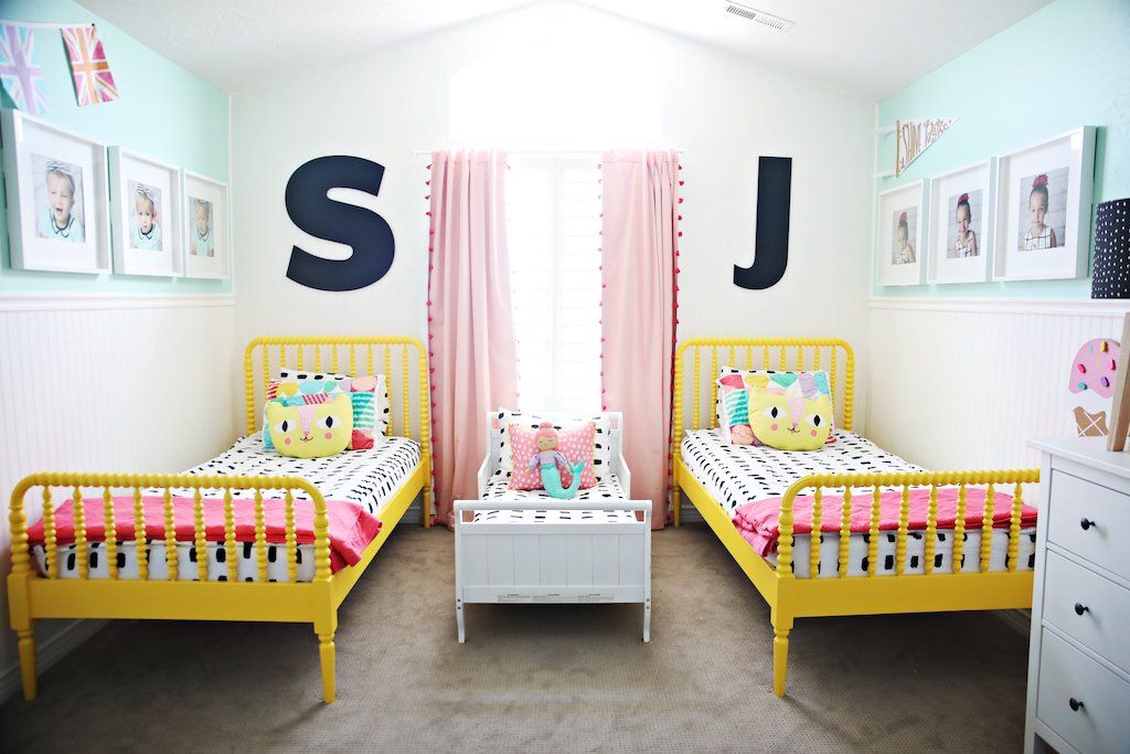 Room with two twin bedframes with white and black dashed lined bedding with cat pillows and coral blankets at the foot of the bed, and a toddler bed in the middle of the room with the same bedding and a mermaid pillow