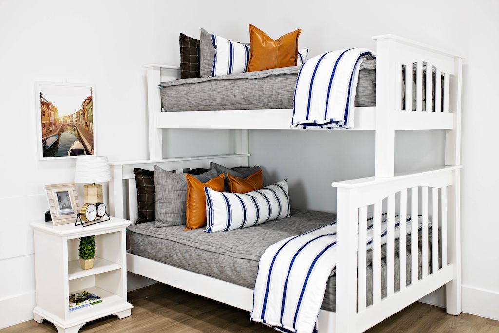 White bunk beds with gray and brown woven bedding, medium brown leather pillows, a white and navy blue striped lumbar pillow and a white and navy blue striped blanket. 