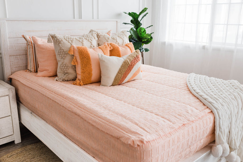 queen bed with Peach bedding with textured rectangle design with dark cream textured euro, orange, textured pillow with tassels, rainbow lumbar and knitted chenille throw with pom poms