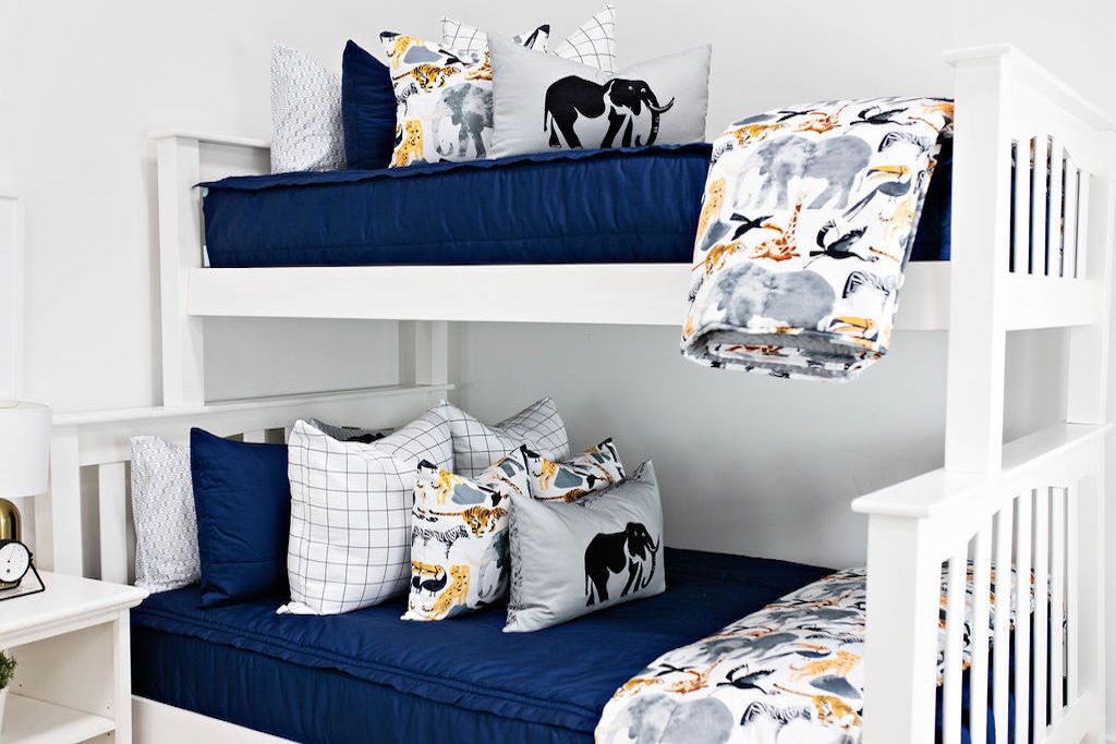 White bunk bed with navy blue bedding, white and black plaid euros, medium pillows with safari animals, gray lumbar with elephant print and blanket with safari animals 