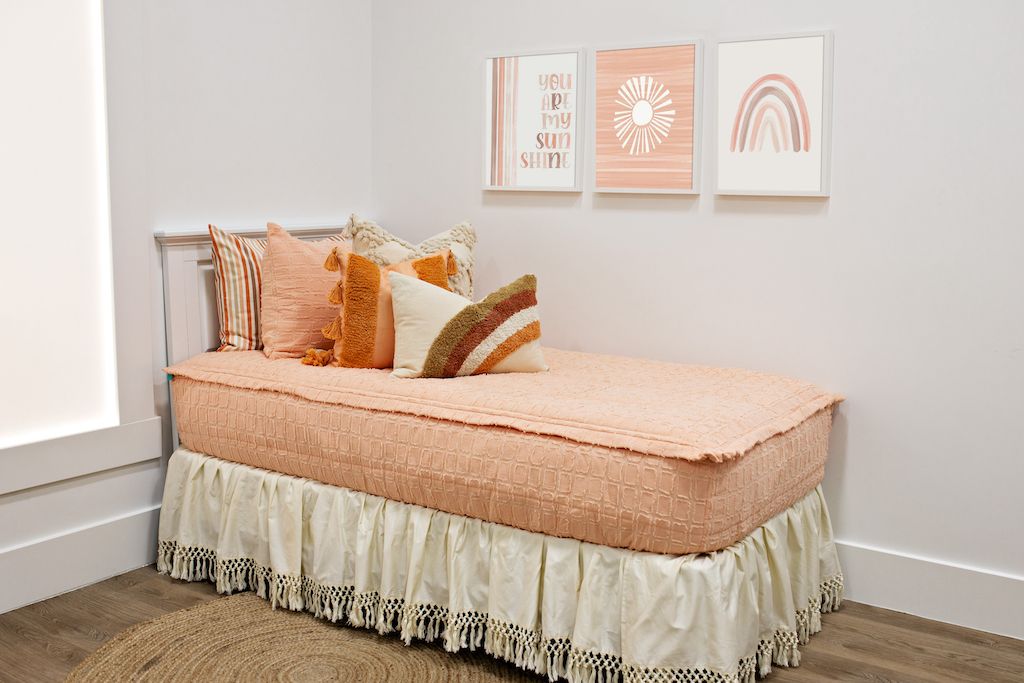 Twin bed with Peach bedding with textured rectangle design with dark cream textured euro, orange, textured pillow with tassels, rainbow lumbar and cream boho bedskirt