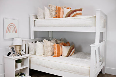 White bunk beds with cream textured bedding, cream textured euro pillows, medium peach textured pillows and a boho rainbow lumbar pillow.  