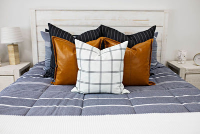 blue and navy striped bedding with deep navy striped euros, faux leather pillows, white and black grid pillow, and white textured blanket with braided tassels