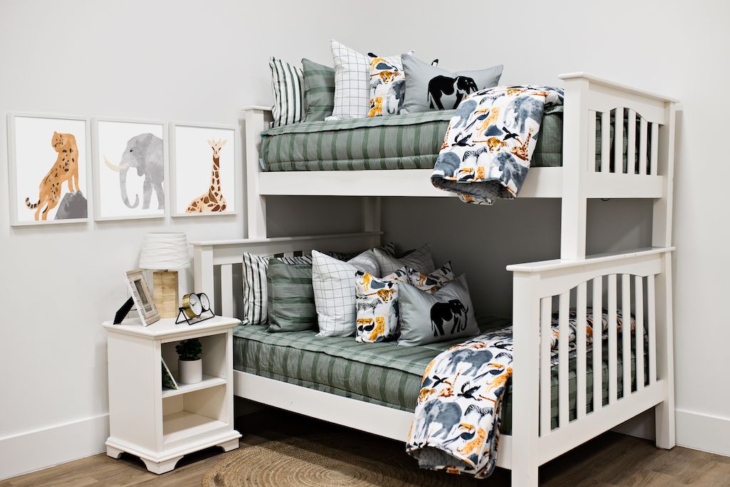 White bunk beds with sage green and white striped bedding, white and black grid pillows, jungle animal pillows, a gray lumbar pillow with an elephant and a blanket with jungle animals. 