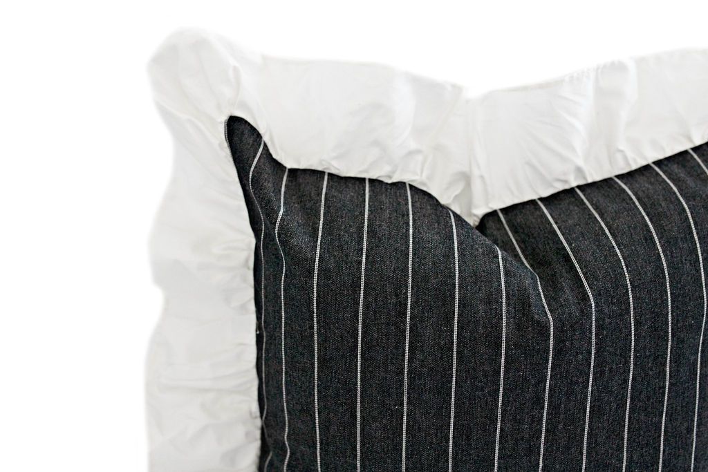 corner of charcoal striped pillow with white ruffle along the edge