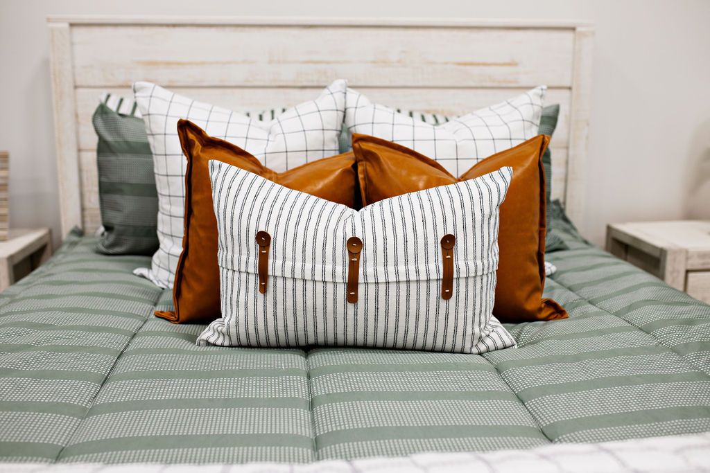 Green striped bedding with two white and black grid euros, two faux leather pillows, white and black striped lumbar with faux lather buckles