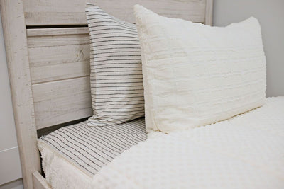 Enlarged view of a white headboard with a cream and gray striped pillowcase and a cream textured sham. 