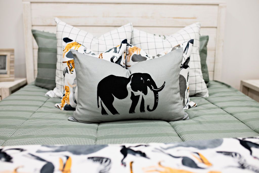 Green striped bedding with two white and black grid patterned euros, two safari animal print pillows, gray lumbar with embroidered elephant and safari animal print blanket