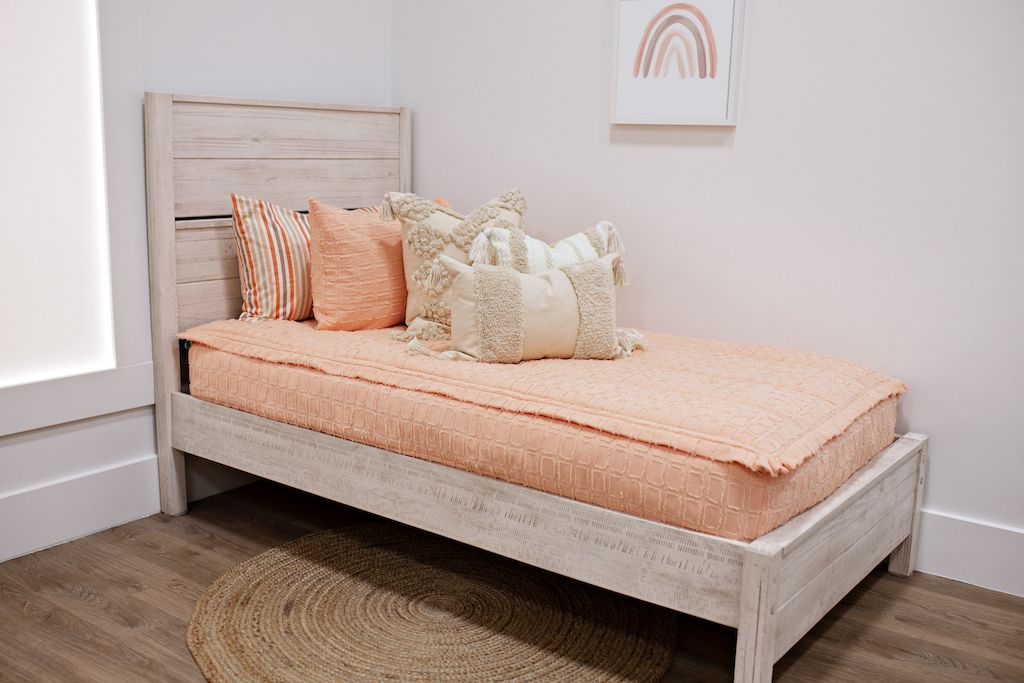 twin bed with peach textured bedding and dark creamy textured euro, a cream and tan woven textured pillow and a textured dark creamy lumbar with tassels