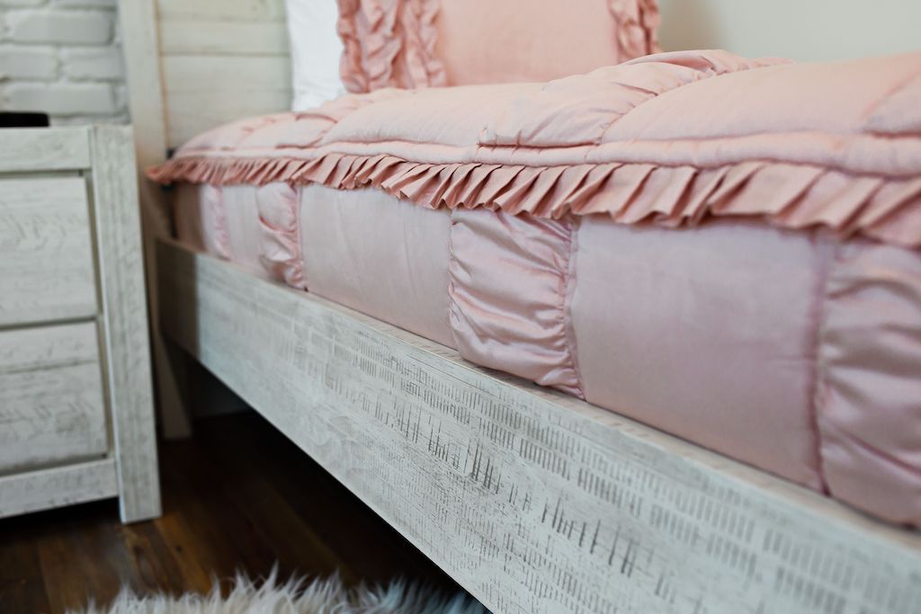 Enlarged side view of blush pink ruffled bedding on a white bed.