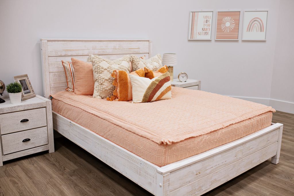 Queen bed with peach bedding with textured rectangle design with dark cream textured euro, orange, textured pillow with tassels, rainbow lumbar 