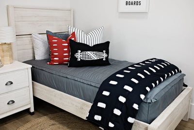 twin bed with gray zipper bedding and White and black striped euro, red and white dashed pillow, black lumbar with white longboard print, black blanket with white dashed lines at the foot of the bed