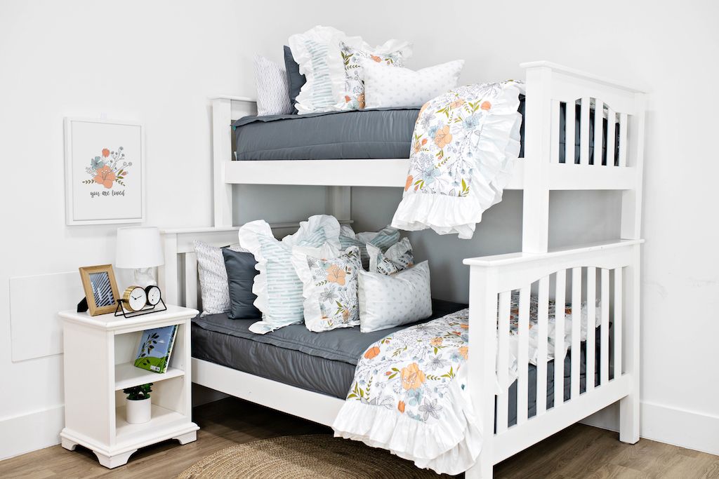 White bunk beds with gray bedding, white and blue striped pillows, multicolored floral pillows, a gray and white lumbar pillow and a multicolored floral blanket.  