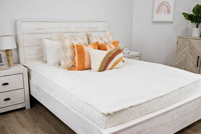 Queen bed with cream textured bedding and dark cream textured euro, orange, textured pillow with tassels, rainbow lumbar 