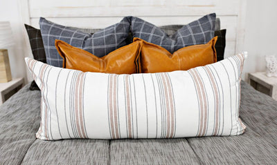 Enlarged view of blue gray and white grid pillows, brown leather pillows, and a cream and cognac striped lumbar pillow.  