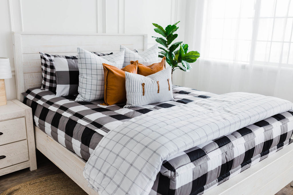 queen bed with Black and white buffalo plaid bedding with white and black grid euro, faux leather pillows, white and black striped lumbar with faux lather buckles and white and black grid pattered blanket